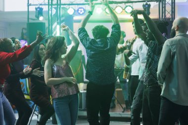 Gece kulübünde parti yaparken dans eden ve el kaldıran aktif insanlar. Elektronik müzik çalan genç erkek ve kadınlar diskotekteki kalabalık dans pistinde dans ediyor ve dinleniyorlar.