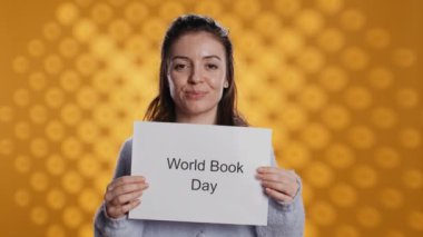 Gülümseyen kitap kulübü üyesi elinde kitap günü mesajı olan bir levha tutuyor. Stüdyonun arka planında izole halde. Okuma yazma bilginin önemini destekleyen ışık saçan kitap kurdu kayıt videosu, kamera B
