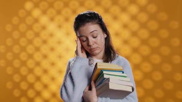 心配した顔の表情を持つ女性は片頭痛を感じ 学校の試験 スタジオの背景のために本を運ぶ あまりにも多くの宿題から頭痛に苦しむ教科書を持つストレスを受けた学生 カメラB ストック映像