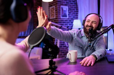 Canlı yayında sunucu kadınla röportaj yapıyor, moda ve tarz trendleri hakkında konuşuyor, fikirlerine katılıyor. İnsan beşliği sosyal medya içeriği oluşturucu, podcast kaydediyor