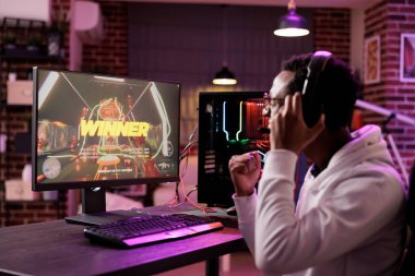 Afrikalı Amerikalı oyuncu diğer oyunculara karşı online çok oyunculu maçı kazanacağı için heyecanlı. Oyun bilgisayarındaki kazanan mesajı neon ışıklarda gören adam oturma odasında