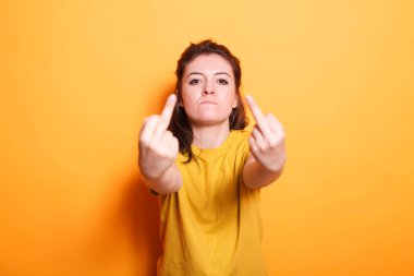 Kendine güvenen esmer kadın, izole arka planda agresif, kaba el hareketleri yapıyor. Orta parmakları kameraya doğru gösteren beyaz kadın portresi.