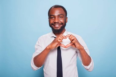 Gülümseyen Afro-Amerikan nüfuzlu hayranları desteklemek için kalp şeklinde parmaklar yapıyor. Beyaz gömlekli ve siyah kravatlı neşeli erkek blogcu göğsünde aşk işareti yapıyor..