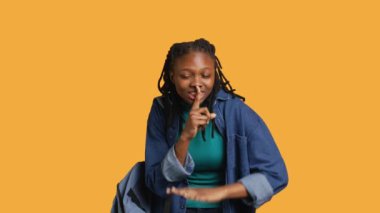 Stern Afrikalı Amerikalı kadın el hareketleriyle şşşş yapıyor, gürültüden rahatsız olmuş, negatif ruh hali içinde. Kız parmaklarını dudaklara koyuyor, sessiz işaret hareketi yapıyor, stüdyo arka planı, kamera A