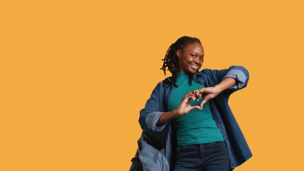 友好的な笑顔のアフリカ系アメリカ人女性の肖像画は 心臓シンボル形のジェスチャーを手で行い 愛情を持っています 愛のジェスチャー スタジオの背景 カメラBを示す陽気な看護人 — ストック動画