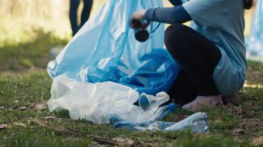 Ormandan çöp ve plastik şişe toplamaktan yorulmuş küçük bir kız gönüllülere çöp toplamada yardım ediyor. Çocuk eylemci çöp torbasında çöp topluyor. Kapatın. Kamera A.