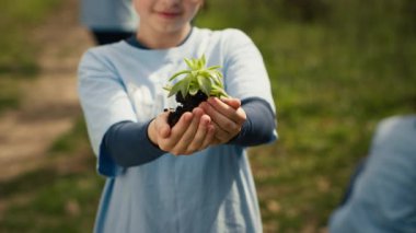 Küçük bir çocuk elinde yeşil bir filizle toprağı tutuyor, çevresel koruma ve doğal yetiştirmeye katkıda bulunuyor. Genç aktivist gezegeni kurtarmak için gönüllü çalışıyor. Kamera A.