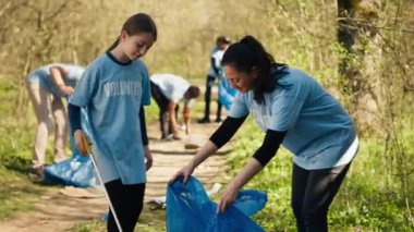 Anne ve çocuk uzun pençe aletleri ve çöp öğütücü poşetleri kullanarak orman bölgesinden çöp topluyorlar. Annesiyle çöp ve plastik atıkları toplayan küçük bir kız, ekolojik adalet. Kamera A.