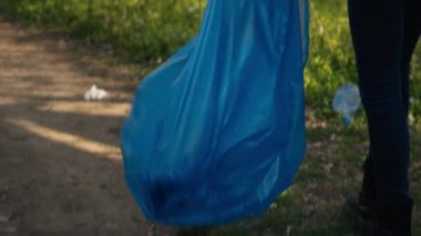 Afro-Amerikalı bir kız çöp torbasında maşa kullanarak çöp topluyor, plastik atıkları geri dönüştürüyor ve ormandaki çöpleri topluyor. Ormanı çöpten temizleyen genç bir kadın eylemci. Kamera A.