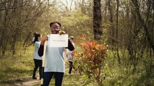 アフリカ系アメリカ人の活動家の肖像画は 私たちの惑星のメッセージを保存し 環境ケアと意識を広めるポスターを保持しています エコロジーの正義と戦うための旗を掲げる若い女性 カメラ — ストック動画