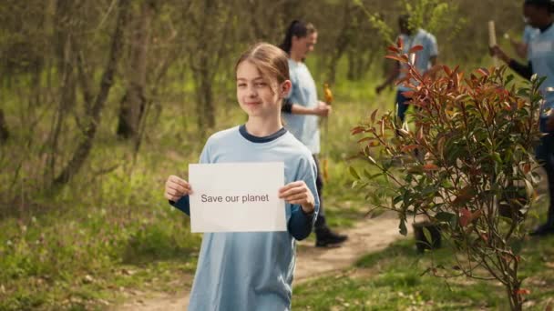 可爱女孩的肖像与拯救我们的星球海报反对污染和非法倾倒 志愿恢复和保护森林中的自然 小孩表现出意识的迹象 相机A — 图库视频影像