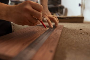 Craftsperson, marangozhanede ahşap mobilya yapımında kullanılan kalasları ölçmek için cetvel kullanıyor. Tahta üzerinde kalem olan ahşap çizim uzmanı nereyi keseceğini belirlemek için, kapat