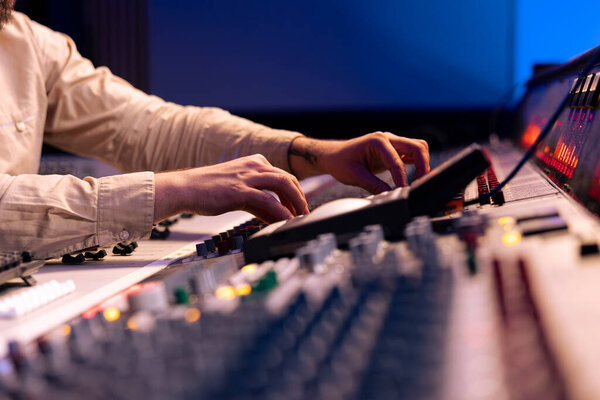 Audio expert uses mixing console and switchers on control room panel, adjusting sound on mixer. Music producer changes recording settings with technical equipment and soundboard.
