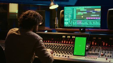 Profesyonel ses uzmanı, müzik stüdyosunda şarkıları karıştırıp ustalaştırıyor kontrol odasında düğmelere ve anahtarlara basıyor. Ses mühendisi melodileri yeşil ekran tabletle kaydediyor. Kamera B.