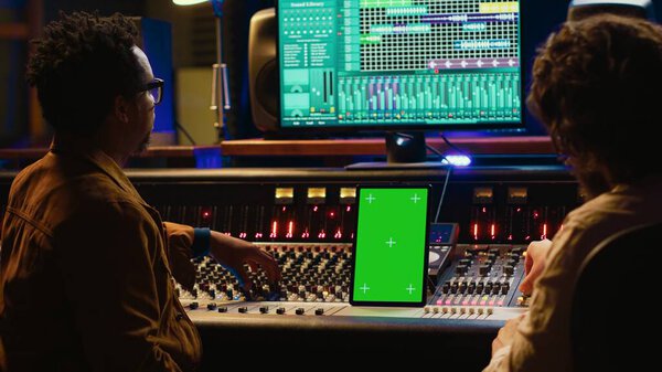 Team of producer and artist use tablet with mockup display in professional studio, mixing and mastering tracks after recording session. Experts working in control room with console. Camera A.