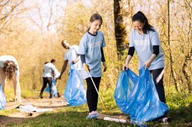 Tatlı anne ve çocuk çöp torbasında çöp ve plastik topluyor, çöpleri geri dönüştürüyor ve orman ekosistemini temizliyor. Doğayı düzene sokmak için annesiyle çalışan genç bir kız..