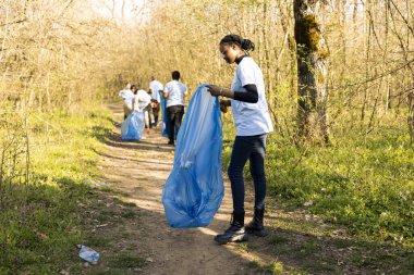 Afro-Amerikalı bir kız çöp poşetinde çöp topluyor, doğa korumasını destekliyor ve çevrenin korunmasına yardım ediyor. Gururlu genç çöp toplamak için gönüllü oluyor..