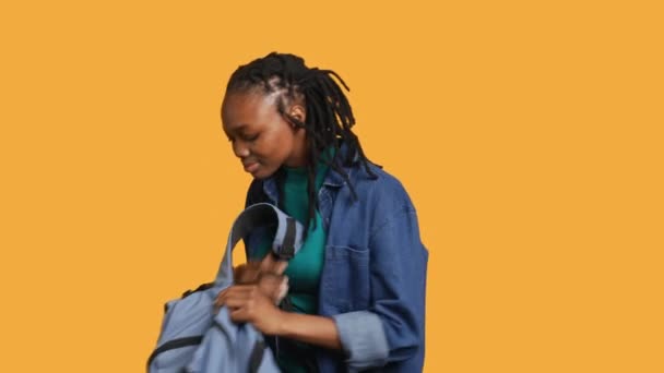 快乐的非洲裔美国女人在背包里翻找 找学校的笔记本 在工作室的背景下被隔离了 快乐少年从背包里拿出大学用品 相机A — 图库视频影像