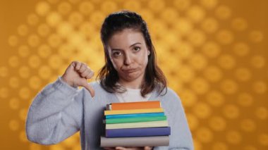 Suratı asık bir kadının portresi kitap yığınını tutuyor, okuma hobisinin tersini gösteriyor. Bir yığın romanı olan asık suratlı kadın el hareketi yapıyor, stüdyo arka planı, kamera B