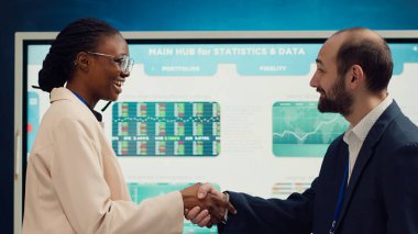 Business manager does handshake with a new employee during a briefing meeting, welcoming her to the team and presenting her to other staff members. Young man shaking hands with trainee. Camera A. clipart