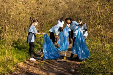 Çeşitli gönüllülerden oluşan bir grup çöp ve plastik atık topluyor, çöp torbalarını orman habitatından çöp toplamak ve geri dönüşüm için kullanıyor. Eylemciler orman alanını çöpten temizlemek için işbirliği yapıyorlar.