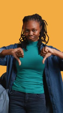 Dikey video görüntüsü hayal kırıklığına uğramış kadın işaret dilini gösteriyor, onaylamıyor, olumsuz geri bildirim sunuyor. Hayal kırıklığına uğramış Afrikalı Amerikalı kız el hareketinden hoşlanmıyor, stüdyo geçmişi, kamera B