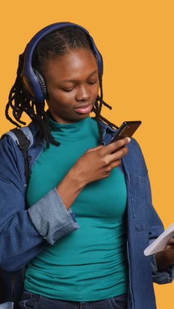 纵向视频非洲裔美国妇女拍摄学校作业的照片 发给同事 听音乐 有工作室背景 学生给试卷拍照 包括考试所需的信息 — 图库视频影像