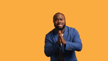 Afro-Amerikalı bir adam dilenci jesti ile el ele veriyor, dilek tutuyor, sarı stüdyo arka planında izole edilmiş bir şekilde. BIPOC çalışanı bir şey istiyor, dua ediyor ve umuyor, kamera B