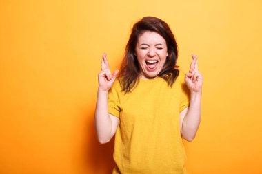Young beautiful brunette woman casually dressed over isolated background having fingers crossed and hopefully smiling with eyes closed. Caucasian lady is excited about winning. clipart