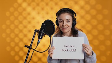 Joyous woman filming promotional video for world book day using microphone, studio background. Happy content creator promoting reading, gaining awareness for literature importance, camera B clipart