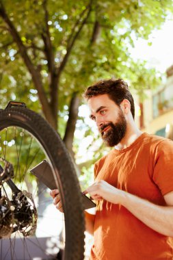 Hevesli sağlıklı erkek bisikletçi, her yıl dijital tabletle lastik bakım rutini olarak lastikleri kontrol ediyor. Kafkasyalı adam hasarlı bisiklet lastiğinin çözümlerini bulmak için akıllı bir cihaz kullanıyor..