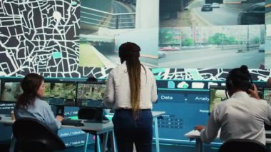 Afrika kökenli Amerikalı yönetici, çeşitli ekibine teslimat paketleri için bilgi sağlıyor. Yollardaki trafiği izleyen insanlar. Kontrol odasında takip emri, koordinatlı uydu haritaları. Kamera B.