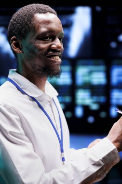 Veri merkezindeki neşeli mühendis yenilenebilir enerji kaynaklarını kullanarak kripto madenciliğini çalıştırıyor. Çevresel etkiyi önleyen çevre dostu sunucu raflarıyla çalışan gülümseyen bir uzman