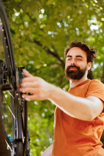 stock image Close-up of young healthy caucasian man examining and adjusting bike wheel rubber and chain outside. Image showing enthusiastic sporty male working on bicycle chain ring in home yard.