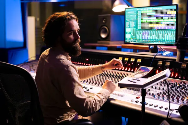 stock image Music technician mixing and mastering songs with motorized faders and knobs, using control desk dashboard and computer. Young sound engineer creating tracks for an album in studio.