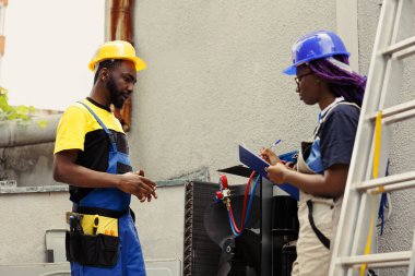 Tecrübeli tamirciler havalandırma ve ısıtma sistemini tamir ediyor. Harici hvac sistemi için yıllık bakım için görevlendirilmiş usta tamirciler, pano üzerine yazı raporları