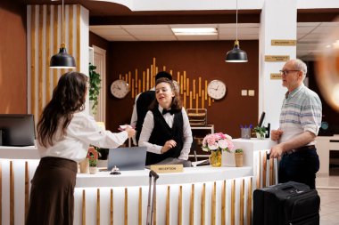 Otel resepsiyonunda, yaşlı erkek ve kadın yolcular kayıt gişesinde rezervasyon prosedürünü bekliyorlar. Emekli son sınıf öğrencisi kadın kayıt için kişisel belgeleri kapıcıya veriyor..