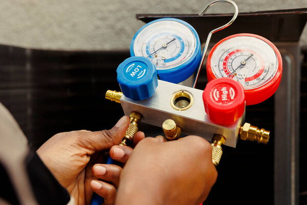Pressure measurement device able to detect damaged expansion valve, freon not circulating properly and other issues. Close up of capable specialist using manifold meter to recondition hvac system