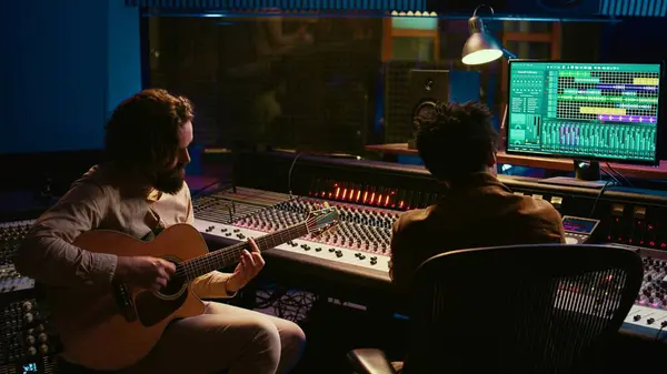 stock image Rockstar recording music on his guitar in professional studio, creating new music for his album in control room. Artist composer producing tracks on electro acoustic guitar. Camera B.