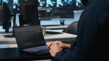 Bilgisayar bilimci veri merkezi sunucularını denetliyor, dizüstü bilgisayarda kod yazıyor, sorun yaratıyor. Yazılım uzmanı ana bilgisayarlarda bakım yapıyor. Not defteri kullanıyor, yakın çekim yapıyor.