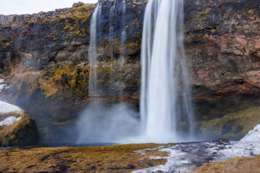 Seljalandsfoss şelalesi, kayalık tepeden taşarak taşar. Kuzey İskandinav topraklarında bir yamaçtan akan nehrin muhteşem panoramik manzarası.