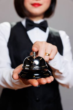 Profesyonel üniforma giyen garson, parmaklarıyla konukseverlik çanına basıyor. Restoran kadın resepsiyonisti yemek alarmını çalıştırıyor, sipariş hakkında sinyal veriyor.