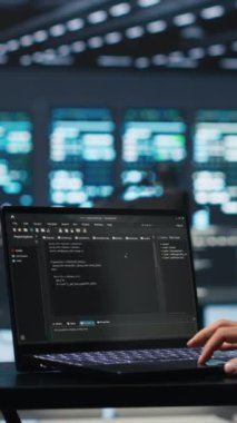 Yüksek teknolojili bir tesiste dizüstü bilgisayara farklı iş yükleri için bilgisayar kaynakları sağlayan dikey video bilgi işlem desteği çalışanı kod yazmakta. Sistem yöneticisi denetlemek için dizüstü bilgisayar kullanır