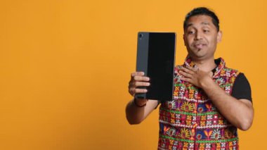 Çevrimiçi video görüşmesinde arkadaşını selamlayan ışıltılı adam, dostça jestler yapıyor. Telekonferansta arkadaş ile iletişim kuran neşeli kişi tablet, stüdyo arka planı, kamera A