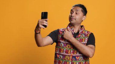 Hintli narsist adam her açıdan selfie çekmek için cep telefonu kullanıyor. Sosyal medya kullanıcısı telefon kamerasıyla fotoğraf çekiyor, mutlu bir şekilde gülümsüyor, stüdyo arka planı, kamera A