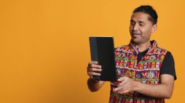 Rahatlamış bir adam, arkadaşıyla internetten görüntülü konuşma yapıyor. Kaygısız Hintli arkadaşla telekonferansta tartışıyor tablet, stüdyo arkaplanı, kamera A 'yı kullanıyor.