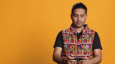 Hintli bir adam cep telefonuyla oyun oynuyor peyzaj modunda, boş zamanların tadını çıkarıyor. Oyuncu cep telefonundan zevk alıyor, eğleniyor, stüdyo arka planında izole edilmiş, kamera A