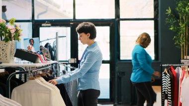 Butik görsel mağazasında çalışan neşeli bir yönetici yeni moda koleksiyonu olan askıları raflara koyuyor. Alış veriş merkezinde modaya uygun ürünler düzenleyen Kafkas tarzı bir çalışan..