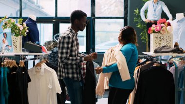 Modern butikte oynaşan, alışveriş sırasında şık ürünlerle oynayan eğlenceli bir çift. Afro-amerikan müşteriler giyim mağazasından şık ürünler alıyorlar. Moda konsepti