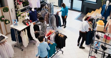 Üst düzey müşteriler şık kıyafetleri kontrol ediyor, modern butikte moda ürünler ve aksesuarlar satın alıyor. Müşteriler askıları yeni moda koleksiyonuyla analiz ediyor